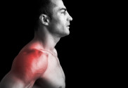 Muscular man suffering with shoulder pain on black background